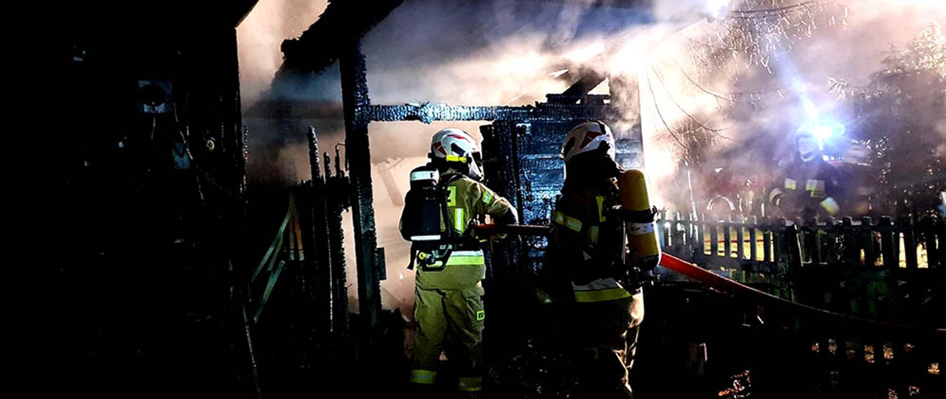 Dwóch strażaków gasi palące się pomieszczenia gospodarcze