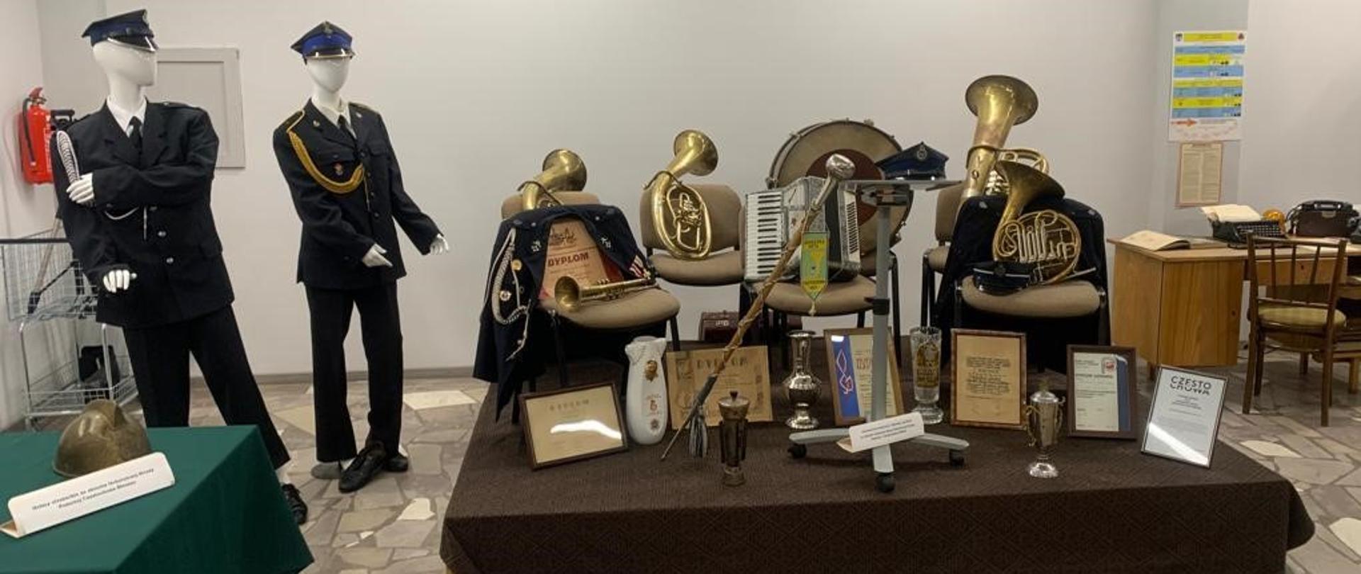 Podest a na nim eksponaty m.in. instrumenty orkiestry strażackiej, buława dyrygencka, dyplomy oraz puchary. Z boku, po lewej, manekiny w mundurach galowych PSP oraz OSP