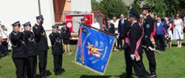Na zdjęciu poczet sztandarowy OSP prezentuje sztandar, któremu honory oddają strażacy OSP oraz Strazak PSP. W tle zaproszeni goście oraz samochód pożarniczy.