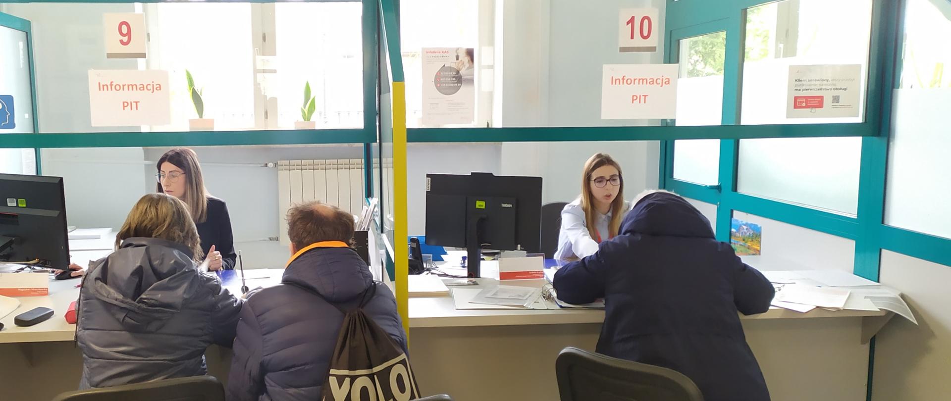Grupa ludzi siedzi przy okienku obsługi w urzędzie.