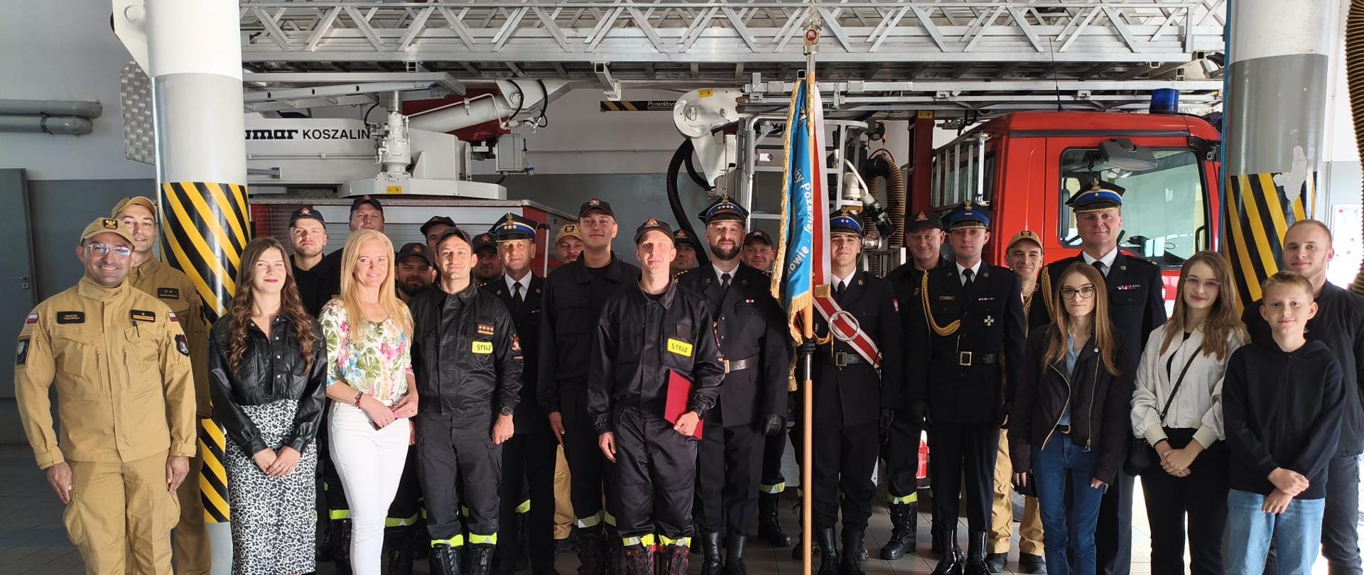 Grupowe zdjęcie nowo przyjętych strażaków z innymi strażakami oraz bliskimi nowo przyjętych strażaków.