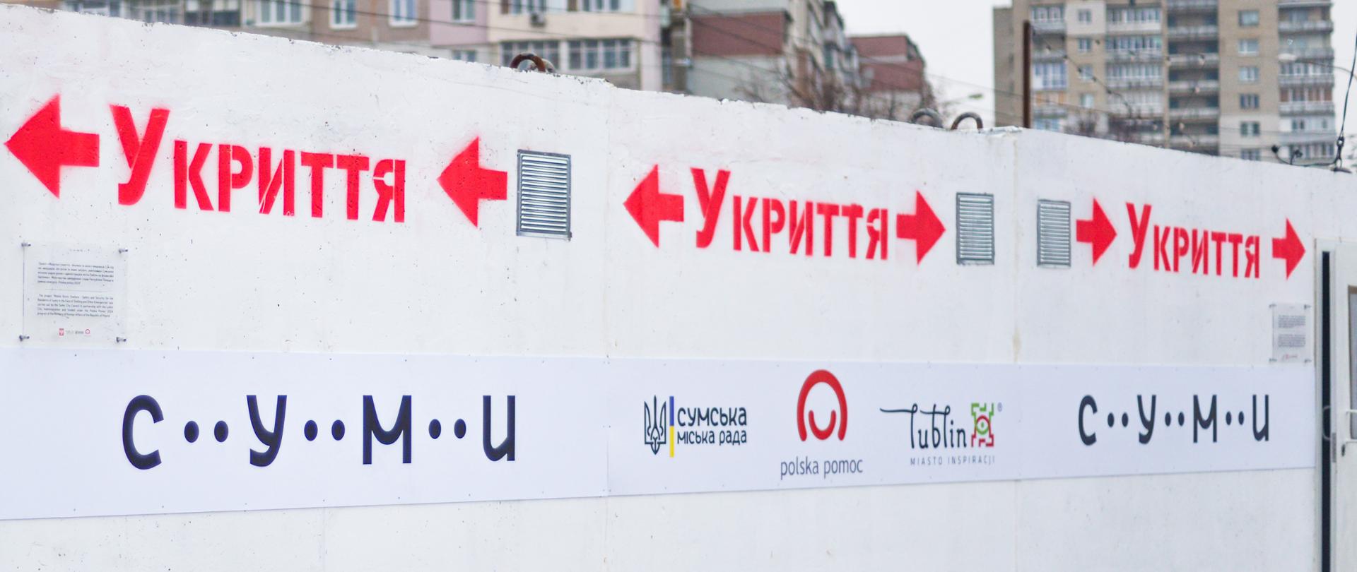 Biała ścian z logo Polskiej pomocy, Lublina, miasta Sumy i czerwonymi napisami w języku ukraińskim Do ukrycia 