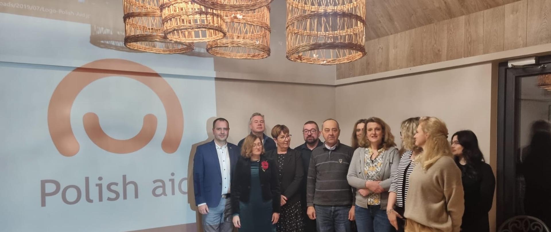 Zdjęcie przedstawia grupę osób pozujących do zdjęcia na tle logo Polish aid