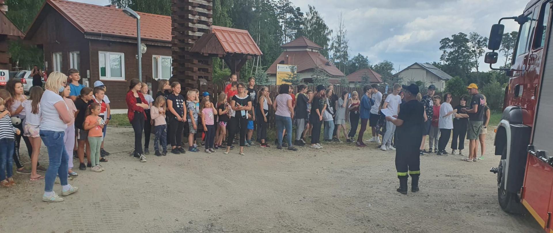 zdjęcie przedstawia grupę dzieci wraz z wychowawcami stojącą przed samochodem strażackim 