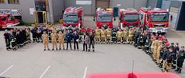 Na zdjęciu widać wszystkich ćwiczących strażaków ustawionych w podkowę, na środku prowadzący ćwiczenia i przedstawiciele zakładu, w tle samochody pożarnicze biorące udział w ćwiczeniach, zdjęcie z lotu ptaka