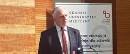 Minister Gowin przemawia do mikrofonu, stoi przy mównicy z logiem GUMed.