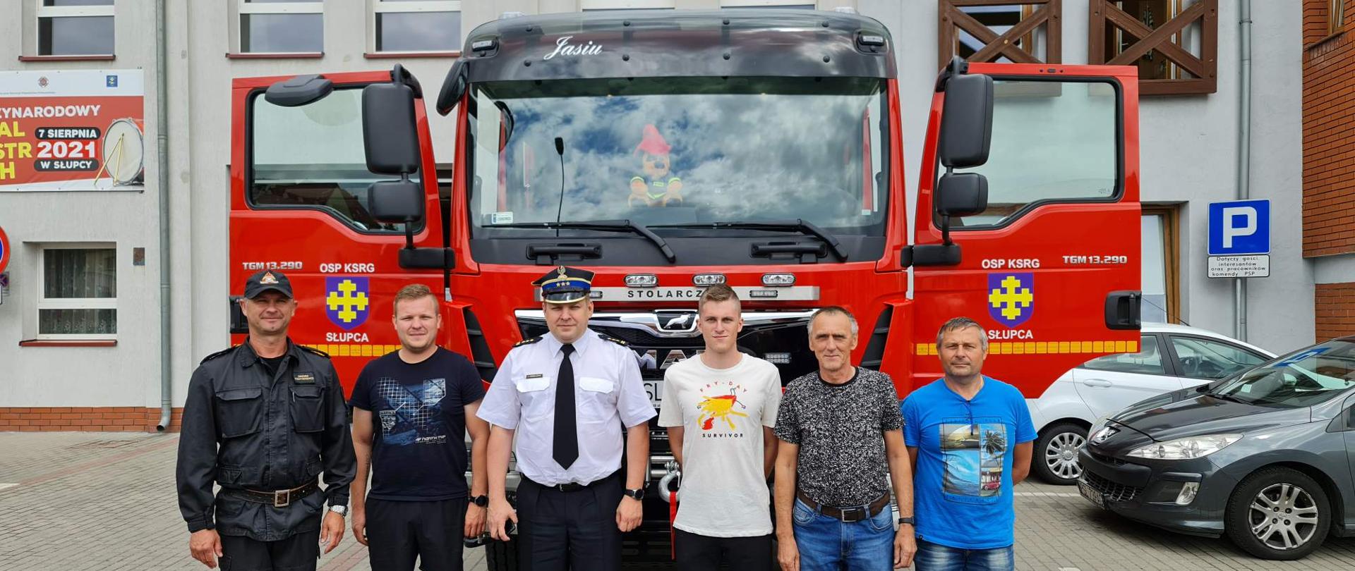 Zastępca Wielkopolskiego Komendanta Wojewódzkiego PSP w Poznaniu wraz z Komendantem Powiatowym PSP w Słupcy oraz z czterema druhami z OSP Słupca stoją na tle samochodu pożarniczego.