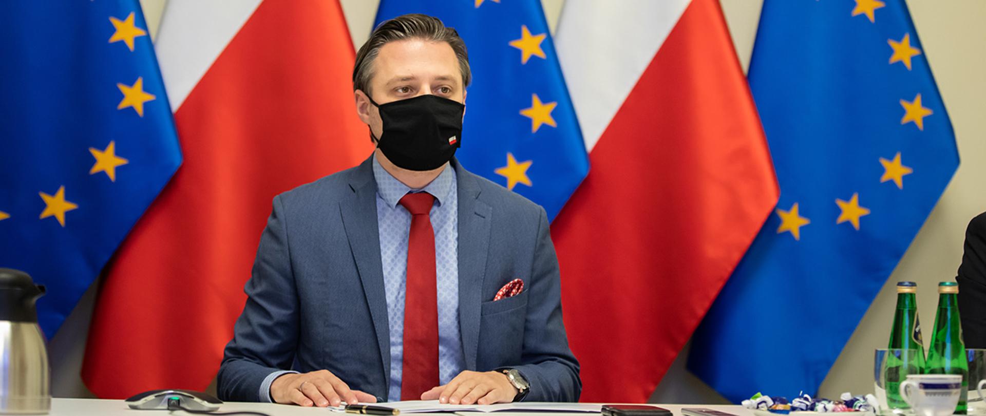 Na zdjęciu widać wiceministra Bartosza Grodeckiego na tle flag Polski i UE.