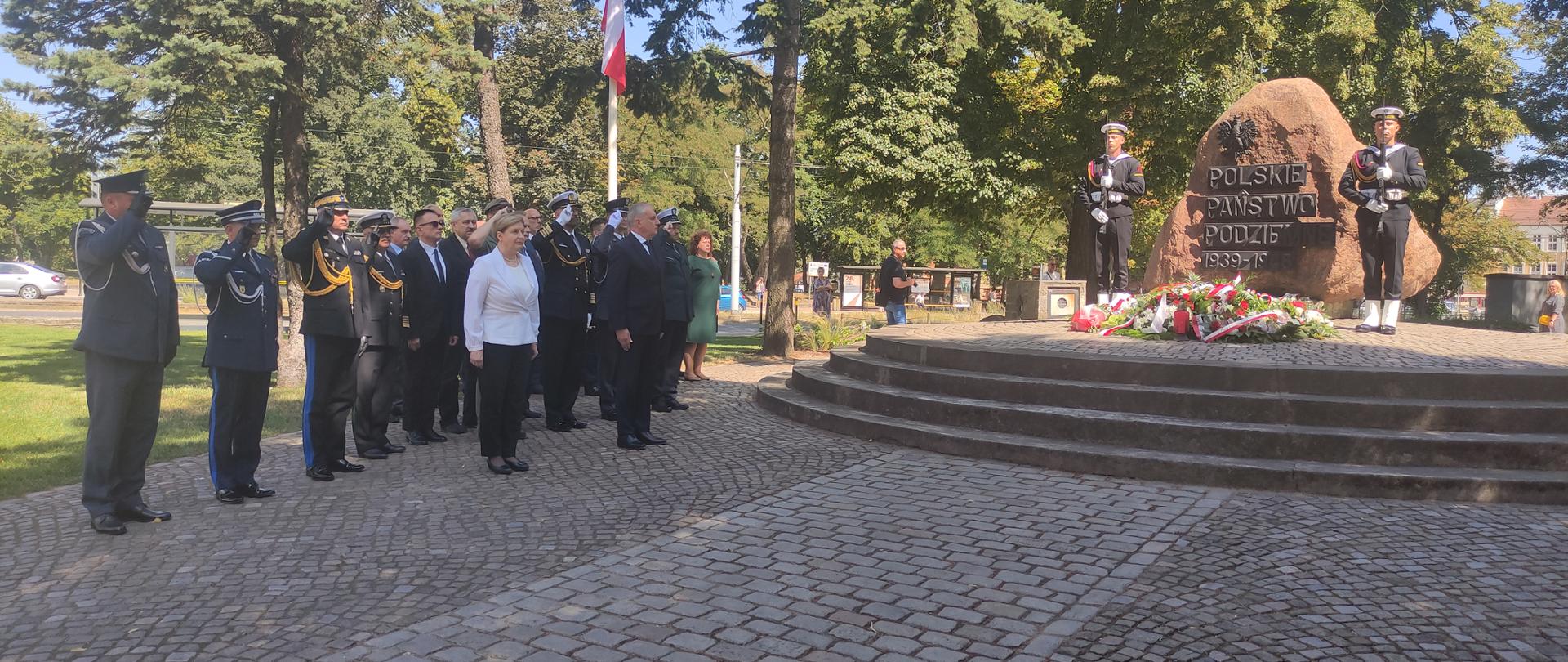 Wojewoda pomorski, zaproszeni goście oraz przedstawiciele służb mundurowych stojąc na baczność przed pomnikiem Polskiego Państwa Podziemnego oddają honor.