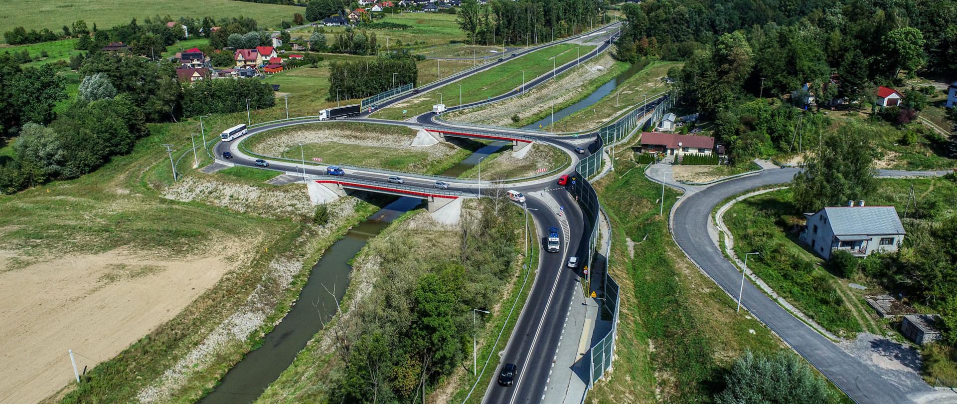 Widok z drona na DK75, na odcinku Łącznik Brzeski, widoczne tereny zielone oraz zabudowa jednorodzinna, w tle pasma górskie
