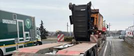 Tył naczepy niskopodwoziowej z załadowaną maszyną ustawiony na platformie wagi drogowej, widoczne tylne światła i tablice ostrzegawcze. Na drugim planie po lewej pojazd Inspekcji Transportu Drogowego.