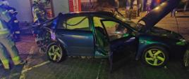 Na zdjęciu widać uszkodzony pojazd osobowy w tle wóz strażacki i strażaków 