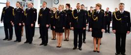 Funkcjonariusze Państwowej Straży Pożarnej stoją w rzędzie podczas uroczystości ubrani w mundury wyjściowe.