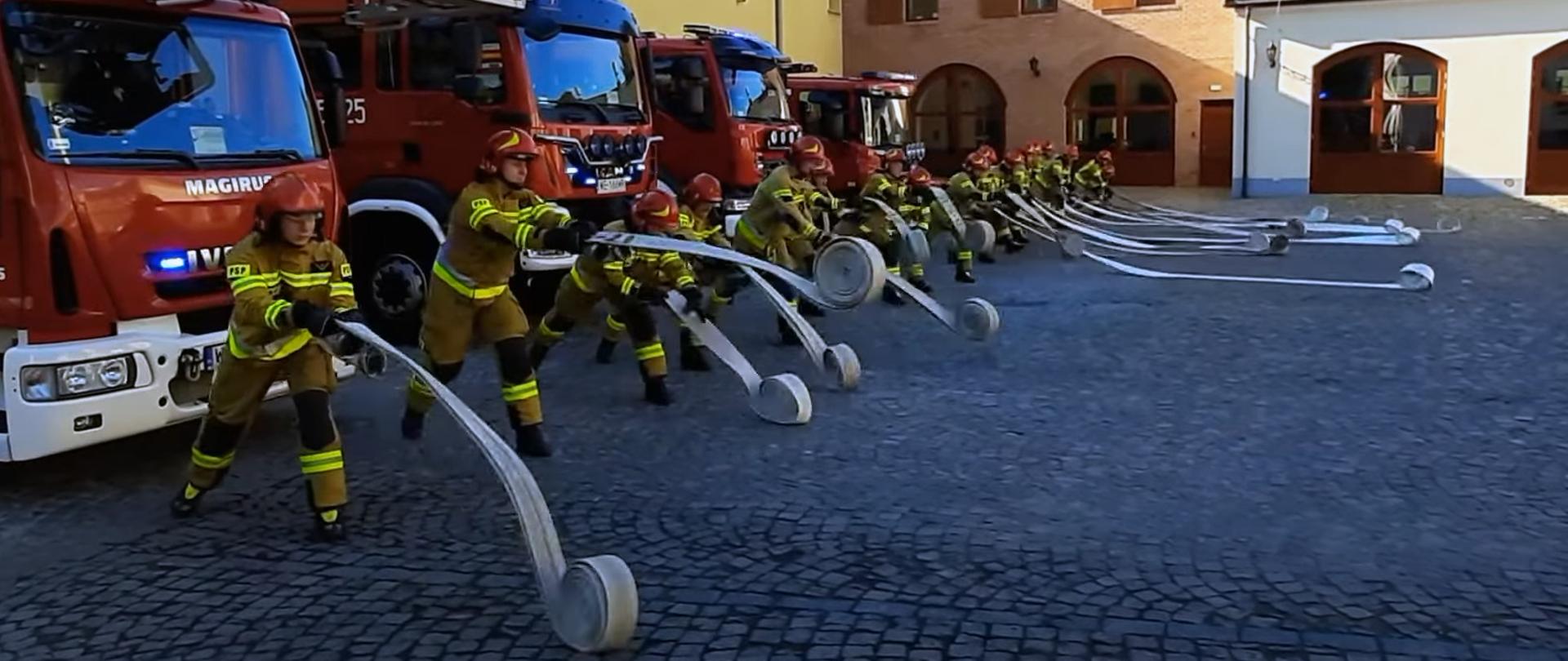 Strażacy na placu przed koszarami rozwijają węże pożarnicze w ramach udziały w akcji UkrainaChallenge