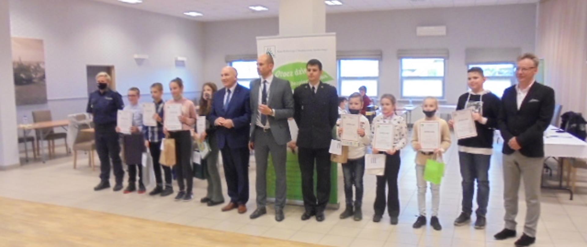 Dzieci z dyplomami ustawione w rzędzie wraz z przedstawicielami władz oraz instytucji publicznych powiatu trzebnickiego. 