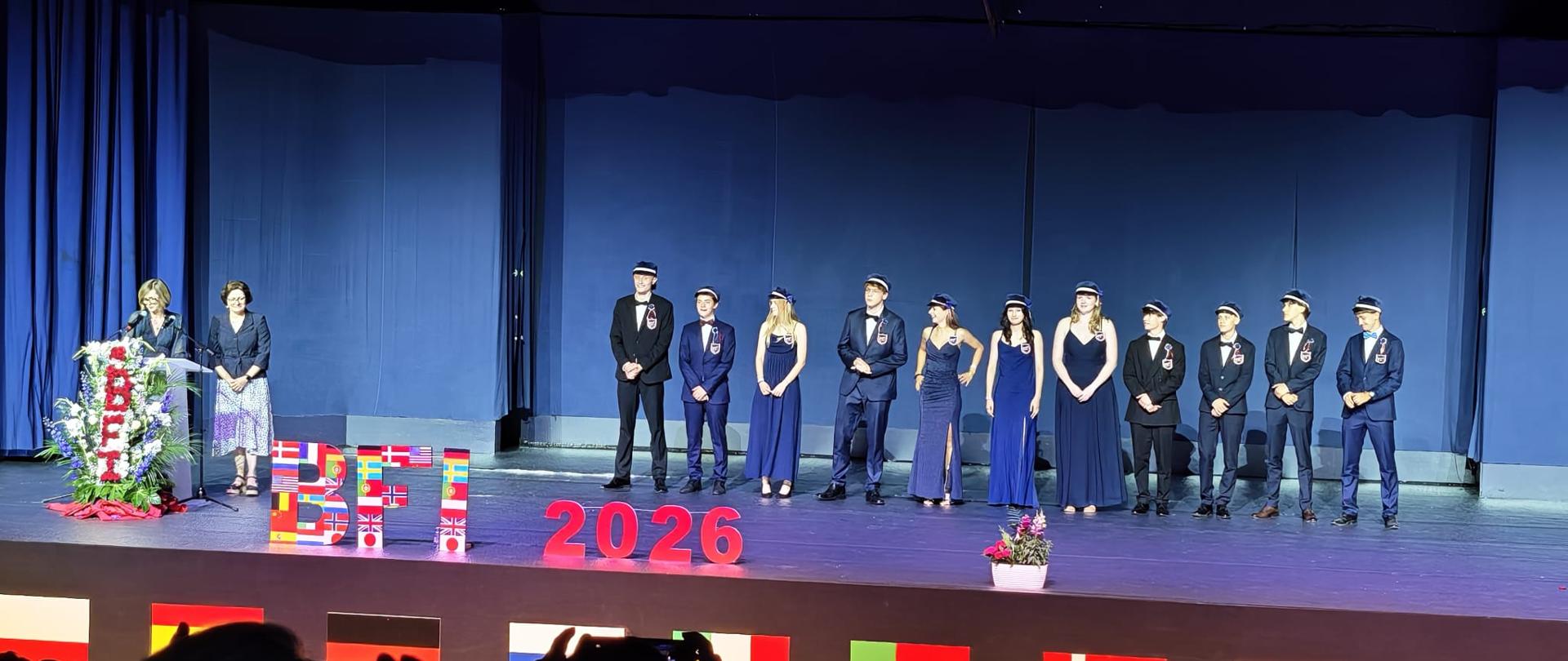 Des jeunes gens en tenue de cérémonie montent sur scène.
