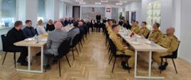 Na zdjęciu widoczny podczas przemówienia Komendant Powiatowy Państwowej Straży Pożarnej w Oleśnie – bryg. Andrzej Wróbel oraz uczestnicy spotkania przedświątecznego, którzy siedzą przy stołach w sali konferencyjnej KP PSP w Oleśnie. Funkcjonariusze ubrani w umundurowanie strażackie.