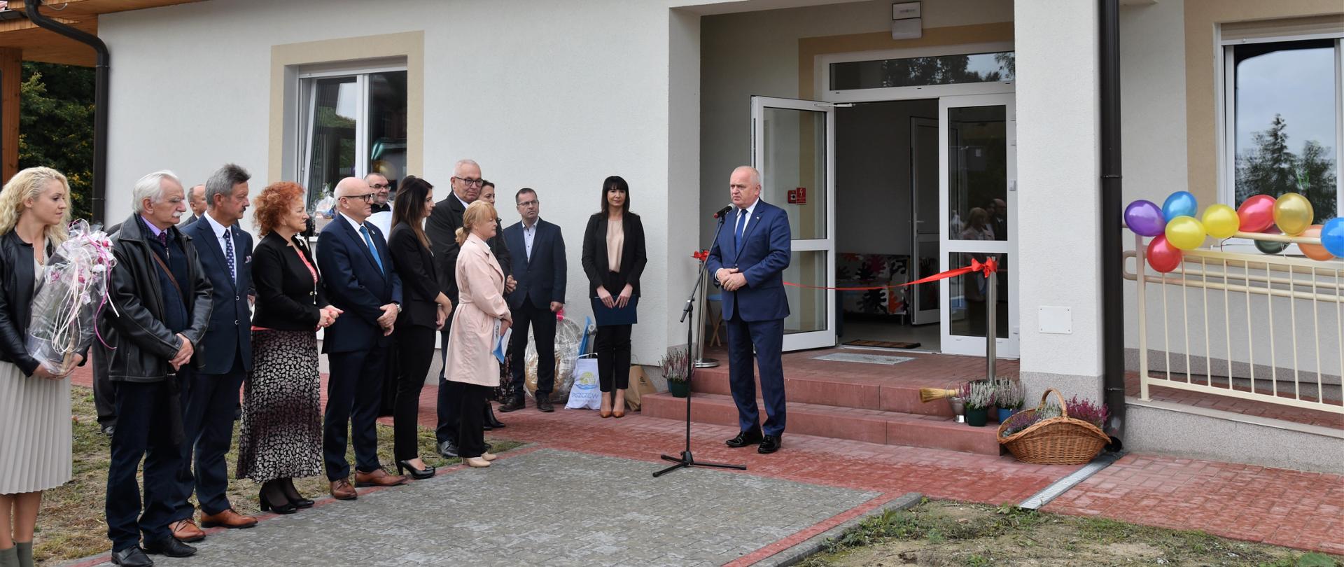 Wojewoda przemawia przed budynkiem Domu Dziecka, po lewej stronie stoją zaproszeni goście uroczystości 