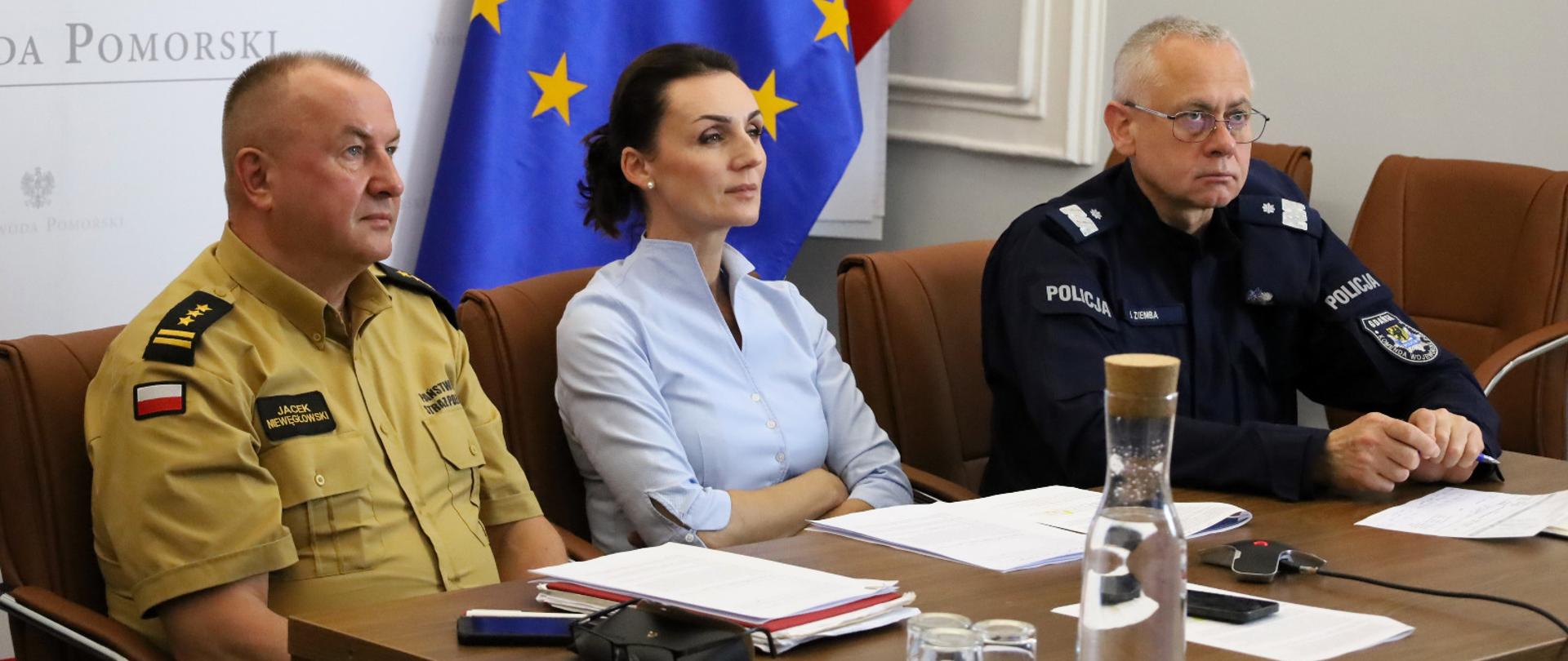 trzy osoby, dwóch mężczyzn w mundurach (strażak i żołnierz) a także kobieta (wojewoda) patrzą na ekran monitora