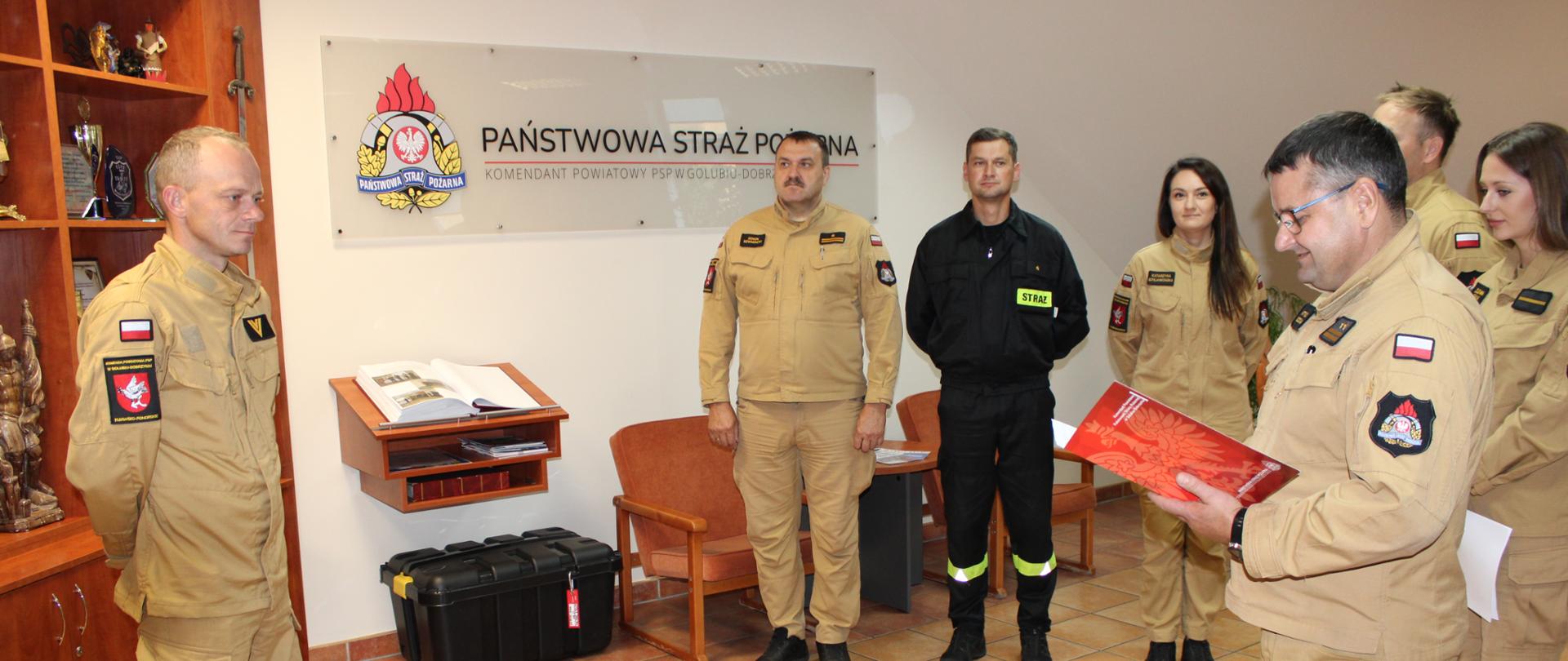 Komendant Powiatowy PSP w Golubiu-Dobrzyniu trzyma w dłoniach teczkę w kolorze czerwonym, przed nim stoi st. ogn. Radosław Dulczewski.