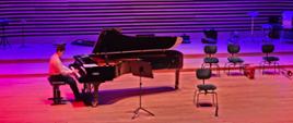 Nastolatek gra na fortepianie Fazioli na estradzie sali koncertowej.