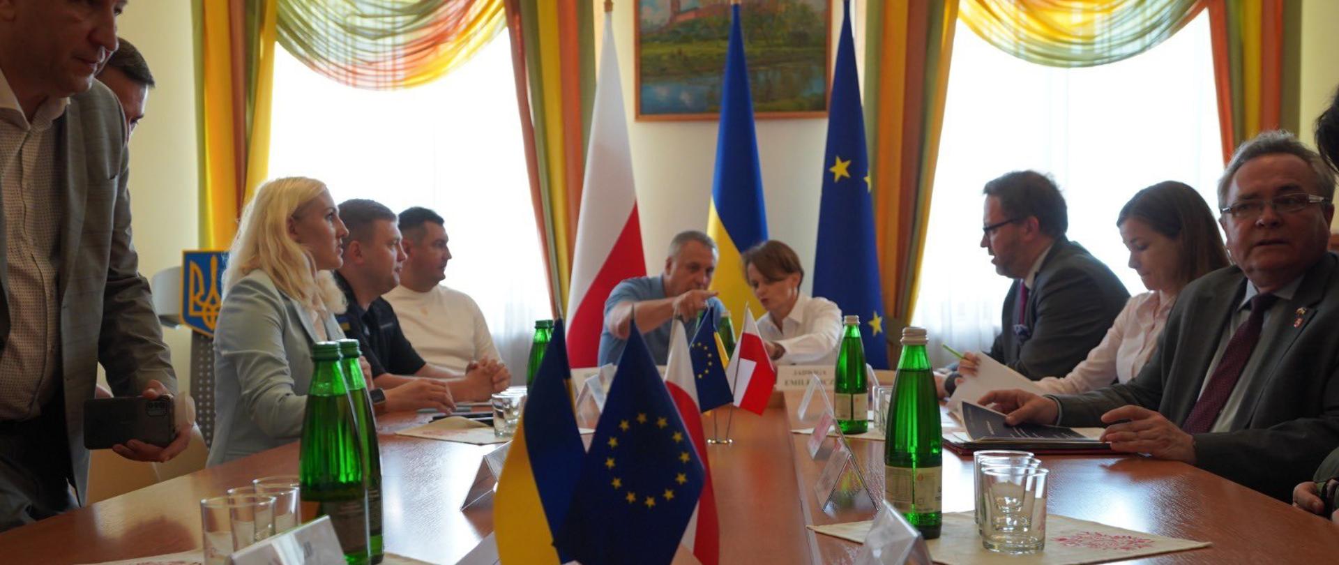 Przy stole siedzi kilka osób, w tym pełnomocnik rządu Jadwiga Emilewicz. Na stole flagi Polski, Ukrainy i UE.