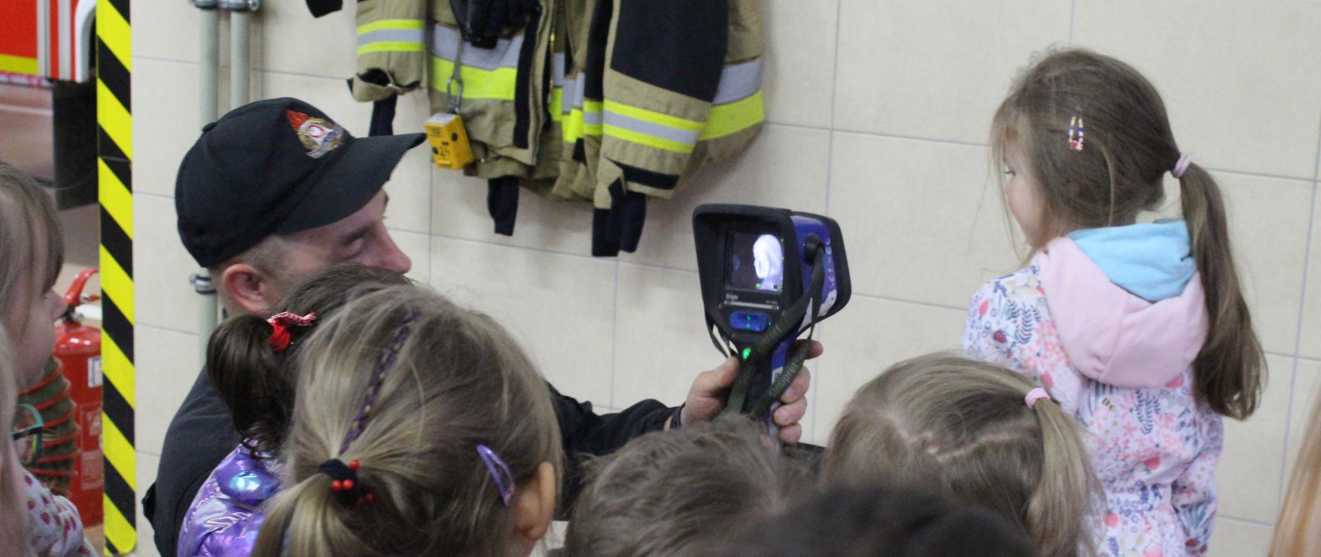 Strażak pokazujący dzieciom z przedszkola widok w kamerze termowizyjnej