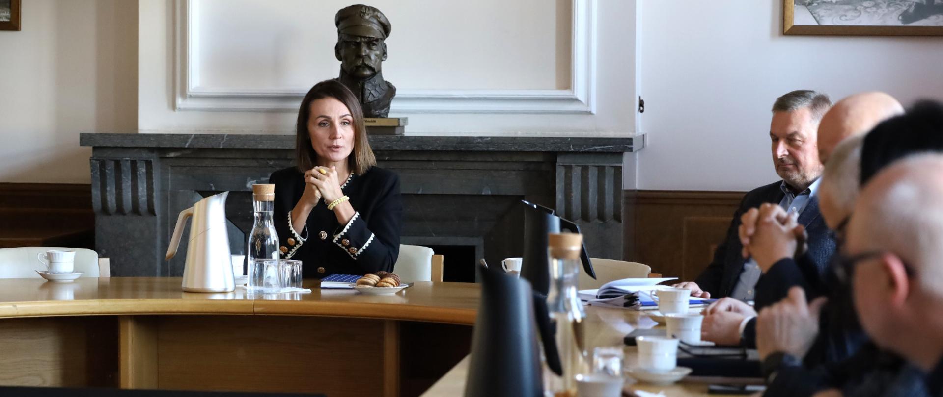 kobieta siedzi przy okrągłym stole i rozmawia z innymi osobami