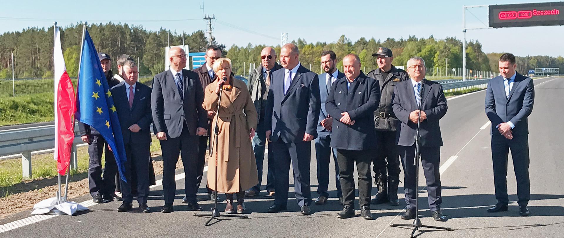 Minister Małgorzata Zielińska stoi przy mikrofonie wśród innych uczestników otwarcia drogi