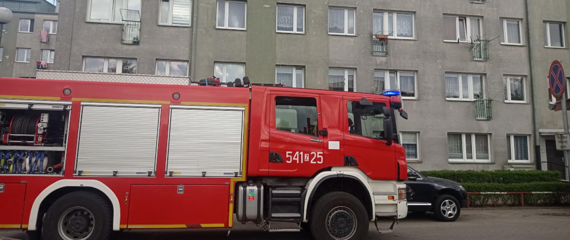 Pożar mieszkania w budynku wielorodzinnym w miejscowości Szczecinek- samochód ratowniczo-gaśniczy koloru czerwonego na tle bloku 
