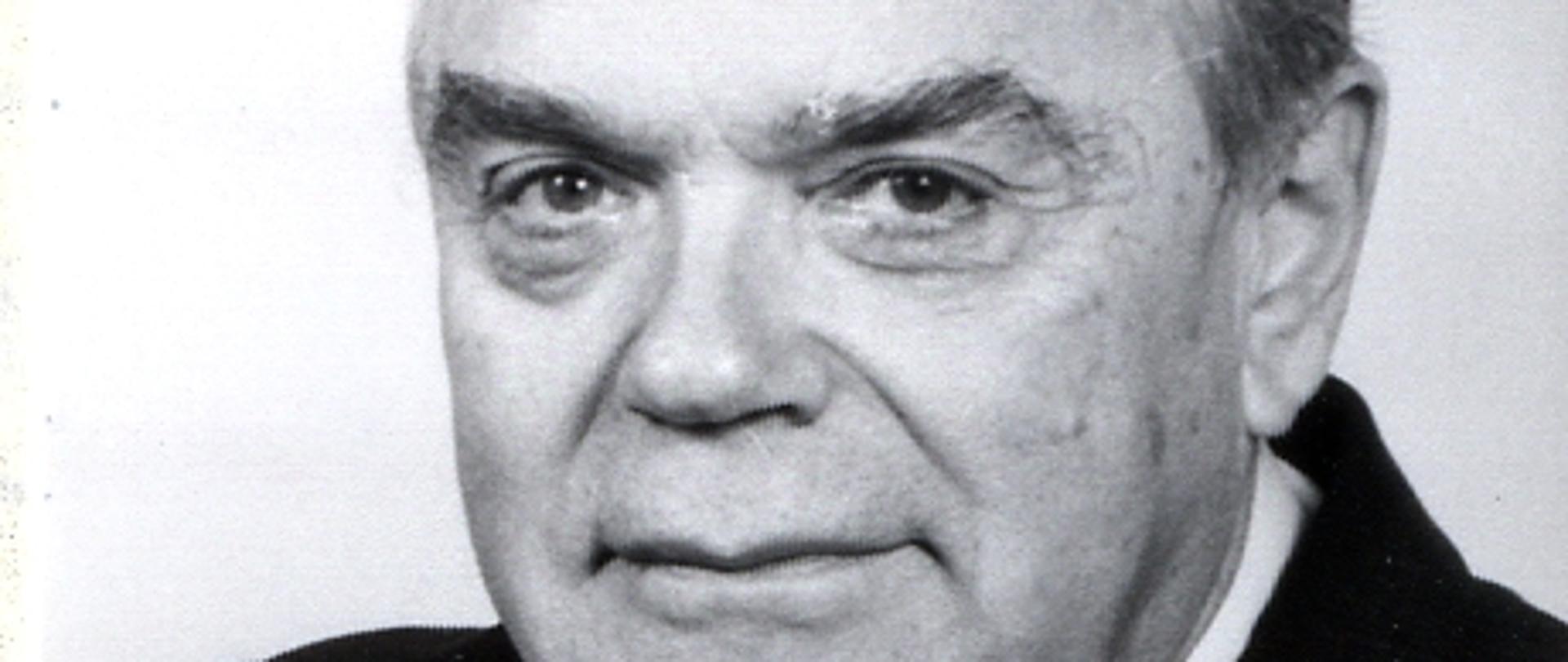 Tadeusz Olechowski- czarno - biały portret mężczyzny, siwe włosy, ciemna marynarka, ciemny krawat, biała koszula.