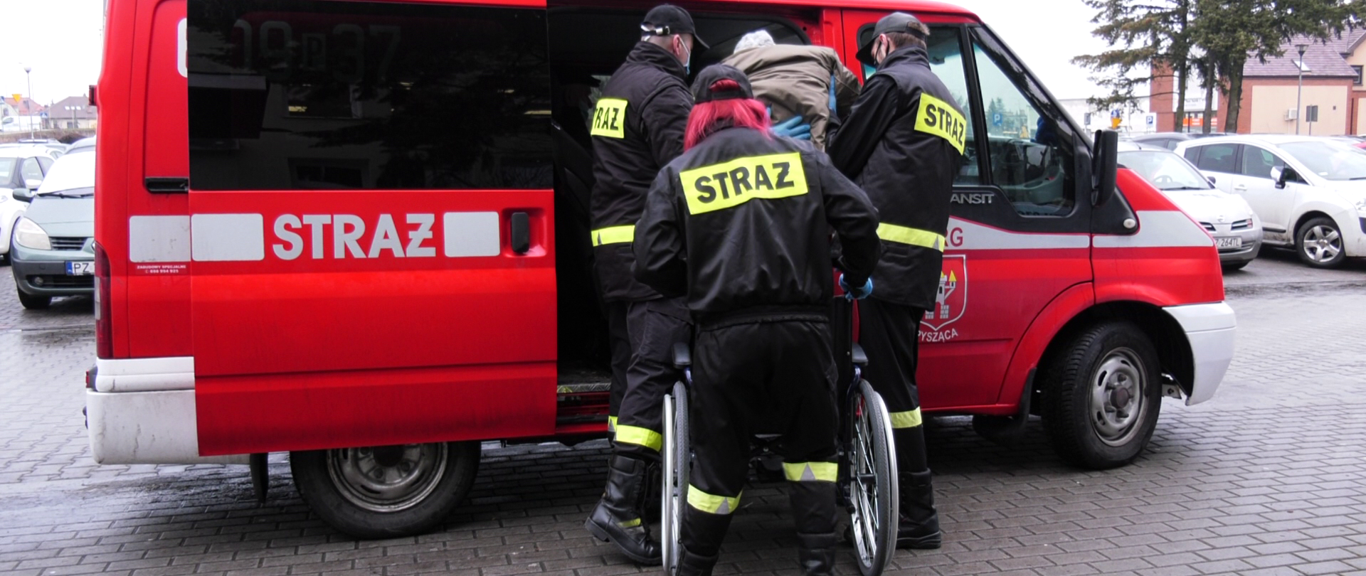 Na zdjęciu strażacy pomagają starszej osobie wsiąść do pojazdu celem transportu do punktu szczepień