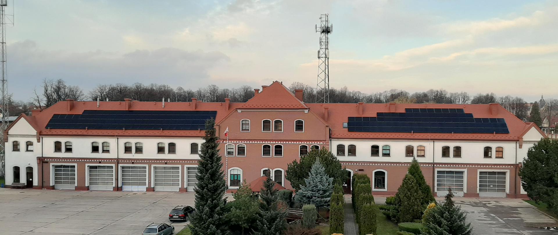 Zdjęcie panoramiczne przedstawiające budynek Komendy Powiatowej PSP w Prudniku, z wykonana instalacja fotowoltaiczną zamontowaną na dachu budynku.