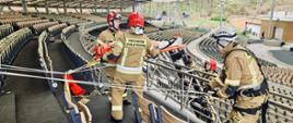 Strażacy za pomocą technik linowych prowadzą ewakuacje poszkodowanego z balkonu.