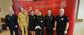 fotografia przedstawia laureatkę wraz z kadrą oraz egzaminatorami konkursu, w tle ścianka Państwowa Straż Pożarna, część wyposażenia Sali