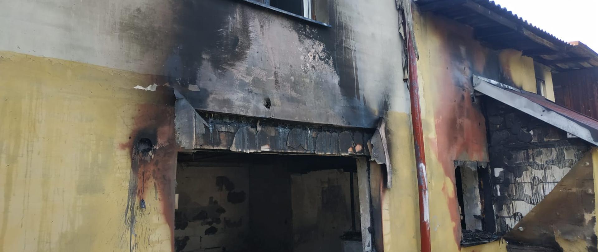 Zdjęcie przedstawia ścianę zewnętrzną spalonej oficyny. Widać zniszczone otwory okienne oraz okopcony tynk.