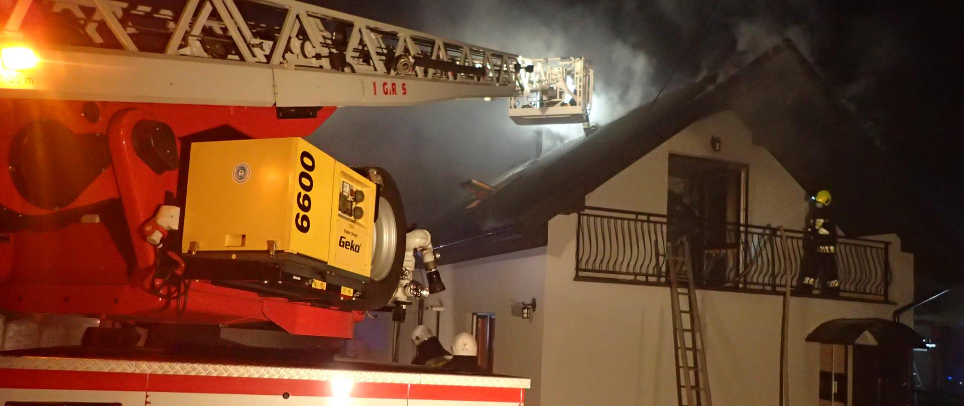 Na pierwszym planie drabina mechaniczna Komendy Powiatowej PSP w Starachowicach oraz ratownicy PSP i OSP gaszący palący się dach. 