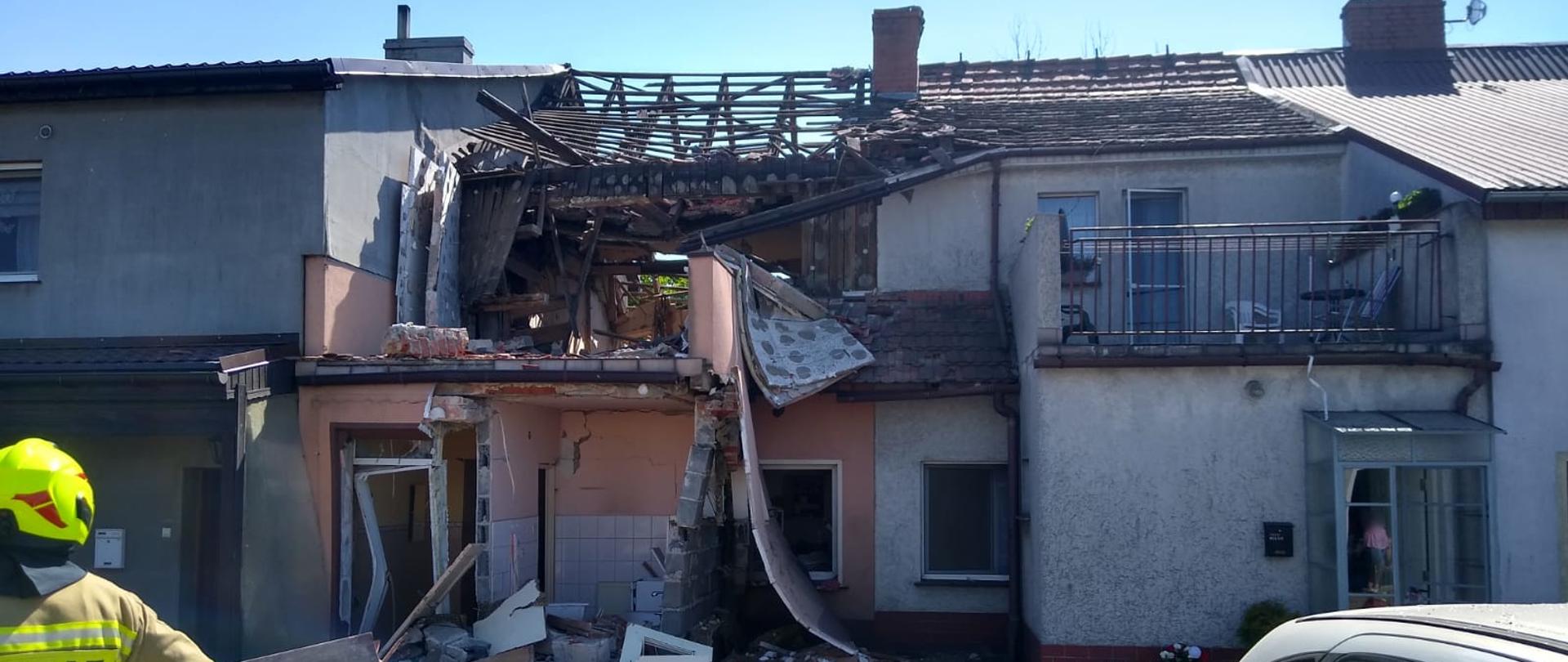 Widoczne miejsce zdarzenia uszkodzone budynki oraz służby ratownicze działające na miejscu zdarzenia.