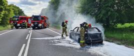 Zdjęcie przedstawia strażaków gaszących pożar samochodu osobowego w miejscowości Kierzkowice.
W tle jezdnia i droga.

