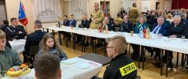Zdjęcie zrobione w pomieszczeniu, podczas spotkania z druhami ochotnikami. Przy stole siedzą zaproszeni goście. Jeden z uczestników spotkania: oficer Państwowej Straży Pożarnej w stopniu generała, stoi i przemawia.