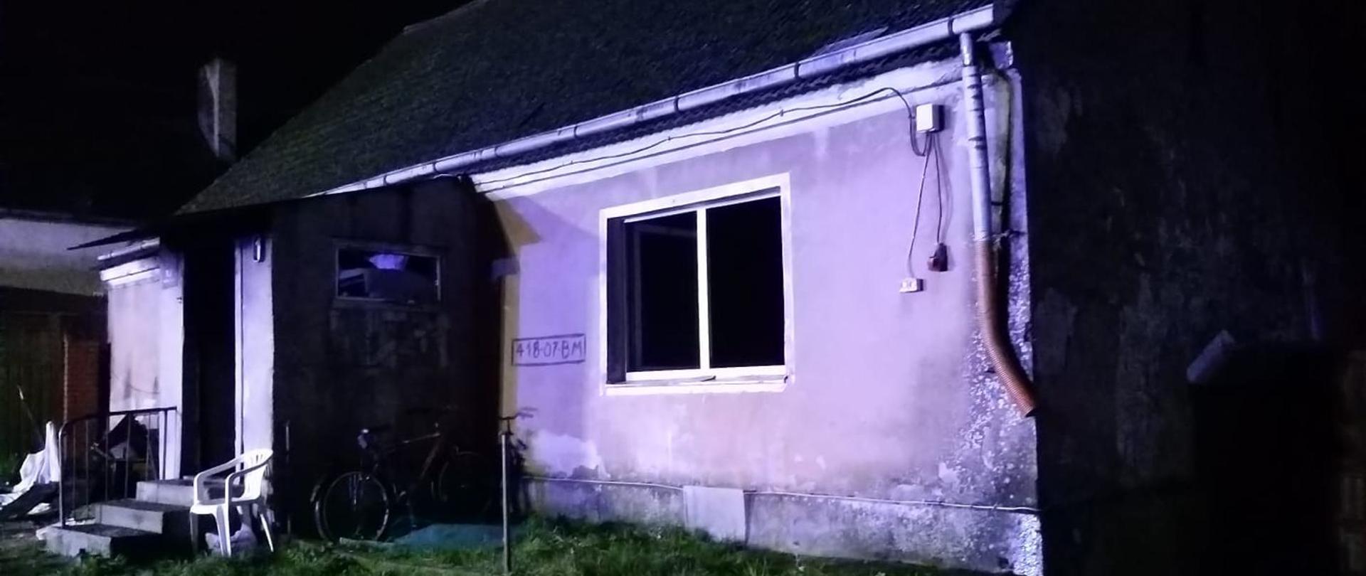 Na zdjęciu widoczny budynek mieszkalny (dom), których był objęty pożarem,. Pora dnia nocna. Przed wejściem do budynku leżą wyrzucone rzeczy, które uległy spaleniu.