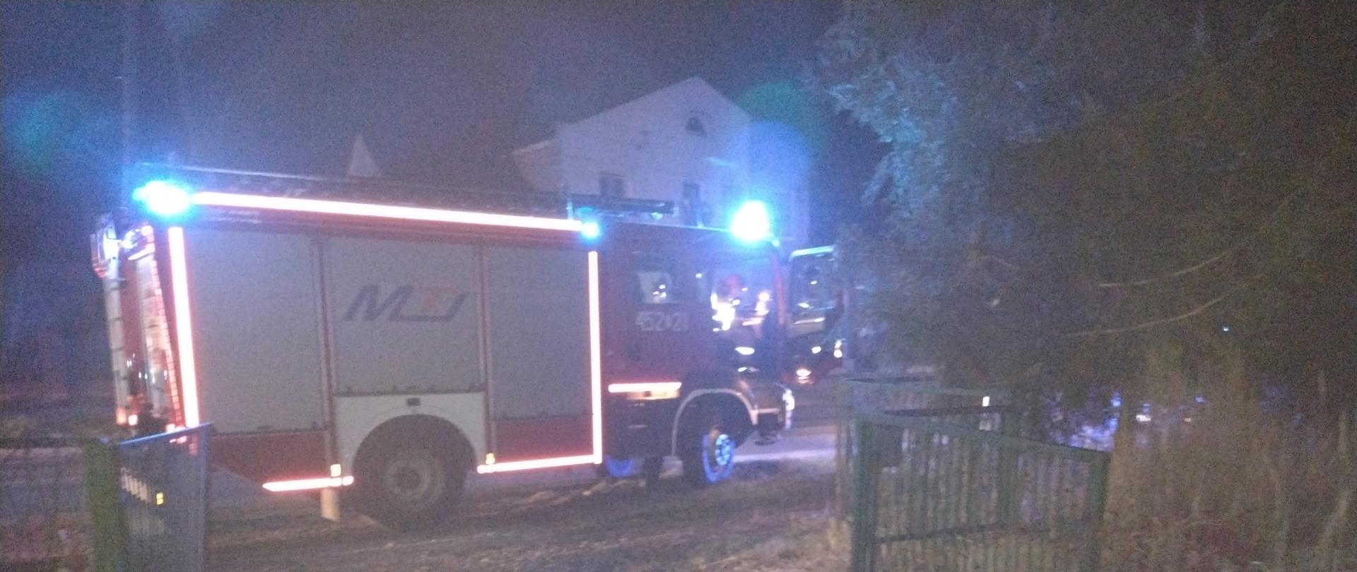 Pora nocna - oświetlony samochód gaśniczy stojący na poboczu przed budynkiem mieszkalnym 