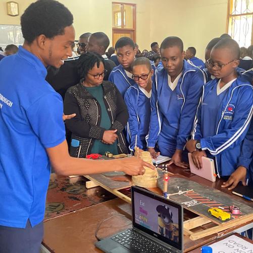 Makieta sygnalizacji świetlnej wokół której stoi grupka uczniów w strojach szkoły oraz nauczycielka