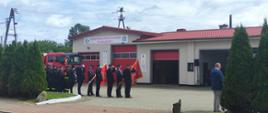 Druhowie Ochotniczej Straży Pożarnej w Rzeczenicy stoją z pochylonymi sztandarami obok stoją inni druhowie na baczność przed nimi stoi samochód gaśniczy.