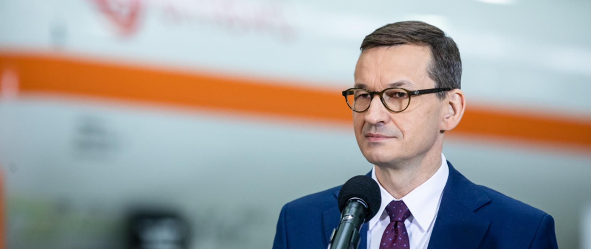 Premier Mateusz Morawiecki stoi przy mikrofonie. W tle maszyna w hali firmy Chemet.