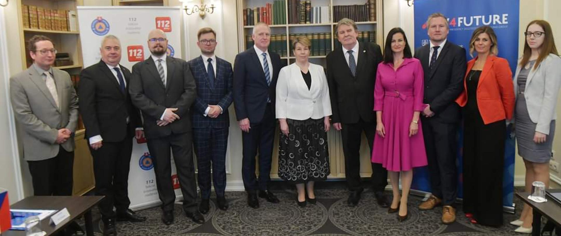 7 mężczyzn i 4 kobiety pozują do zdjęcia pamiątkowego na tle biblioteczki