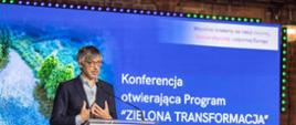 The frame shows a close-up of a screen and a man at a lectern during the opening conference of the "Green Transition" Programme. Krzysztof Bolesta, Secretary of State, Ministry of Climate and Environment Republic of Poland, is speaking.
