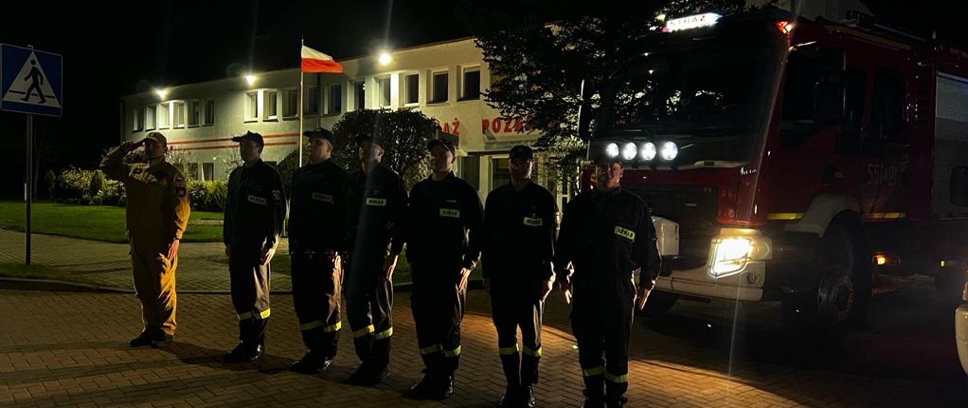 Zdjęcie przedstawia strażaków stojących w szeregu oddających hold zmarlemu strażakowi