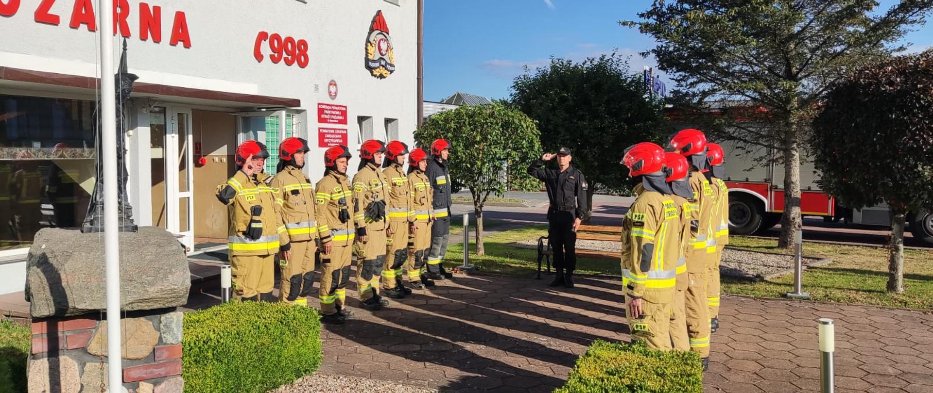 Zdjęcie przedstawia zmianę służby przy fladze. Strażacy oddają hołd tragicznie zmarłemu strażakowi