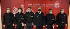 Zdjęcie przedstawia strażaków, którzy stoją przed banerem komendy. Strażacy otrzymali awanse na wyższe stanowiska służbowe. 